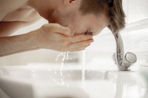 Mann wäscht sich Gesicht mit klarem Wasser.